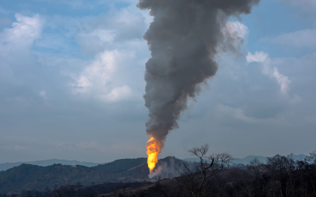 Aerial view of a burnt oil well area with dark smoke and scorched vegetation